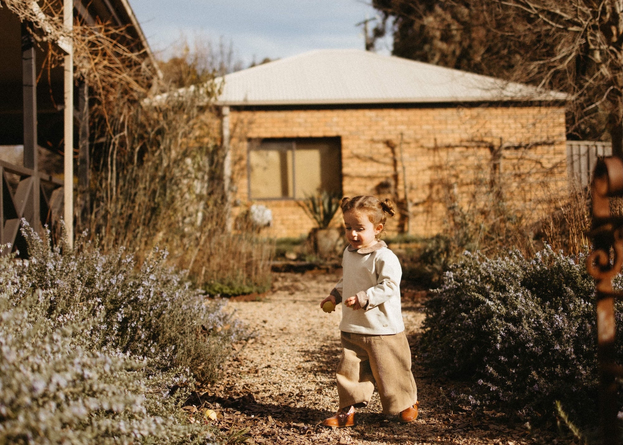 Child walking on a path in a garden with rustic buildings in the background